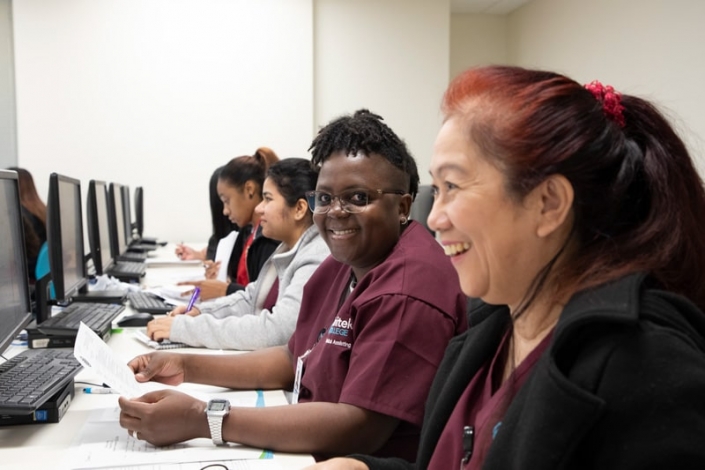 Diverse group of students laughing and studying in a computer lab.