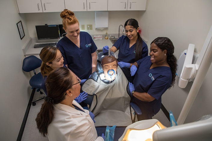 Dental assistant students gathered around a simulation mannequin