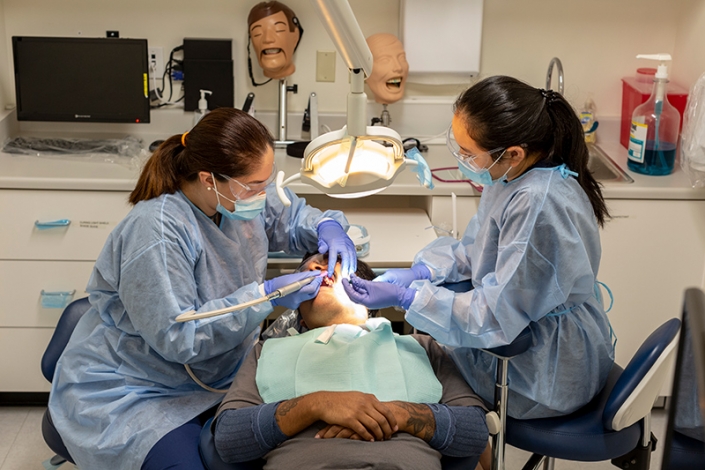 Two dental assistant students practicing dental skills on a real patient.