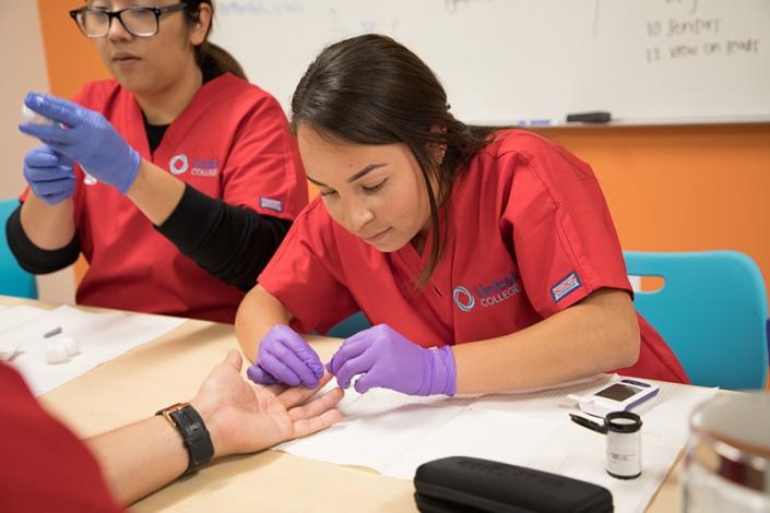 Estudiante de enfermería practicando control de azúcar en sangre en otro estudiante