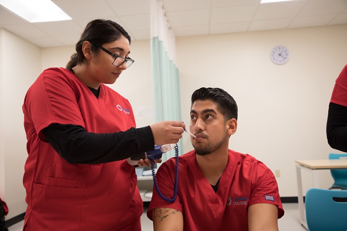 Nursing student practicing taking the temperature of another student.