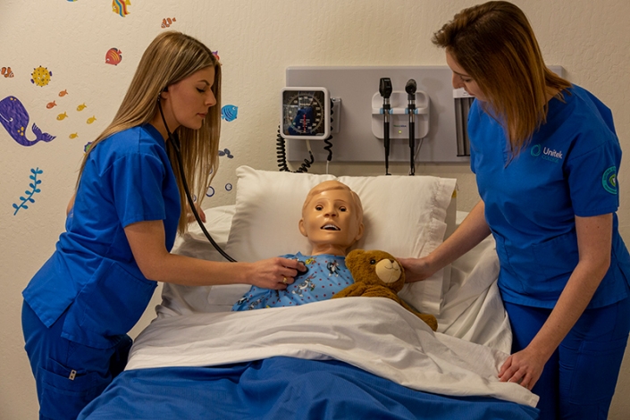 Dos estudiantes de enfermería practicando habilidades en un maniquí de simulación infantil