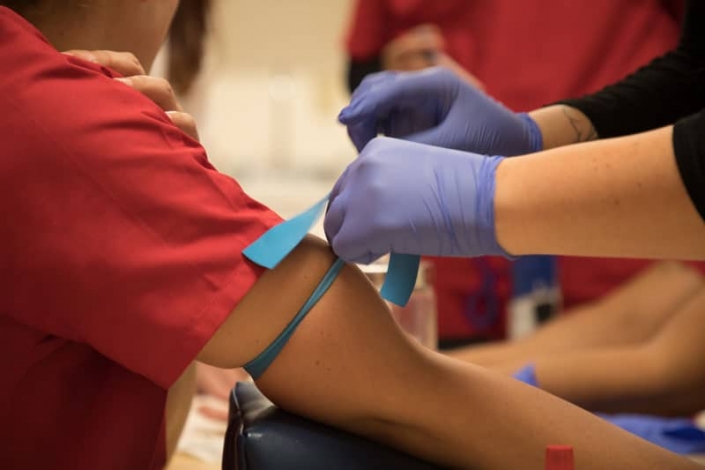 Estudiante de enfermería preparándose para recolectar muestras de sangre de otro estudiante