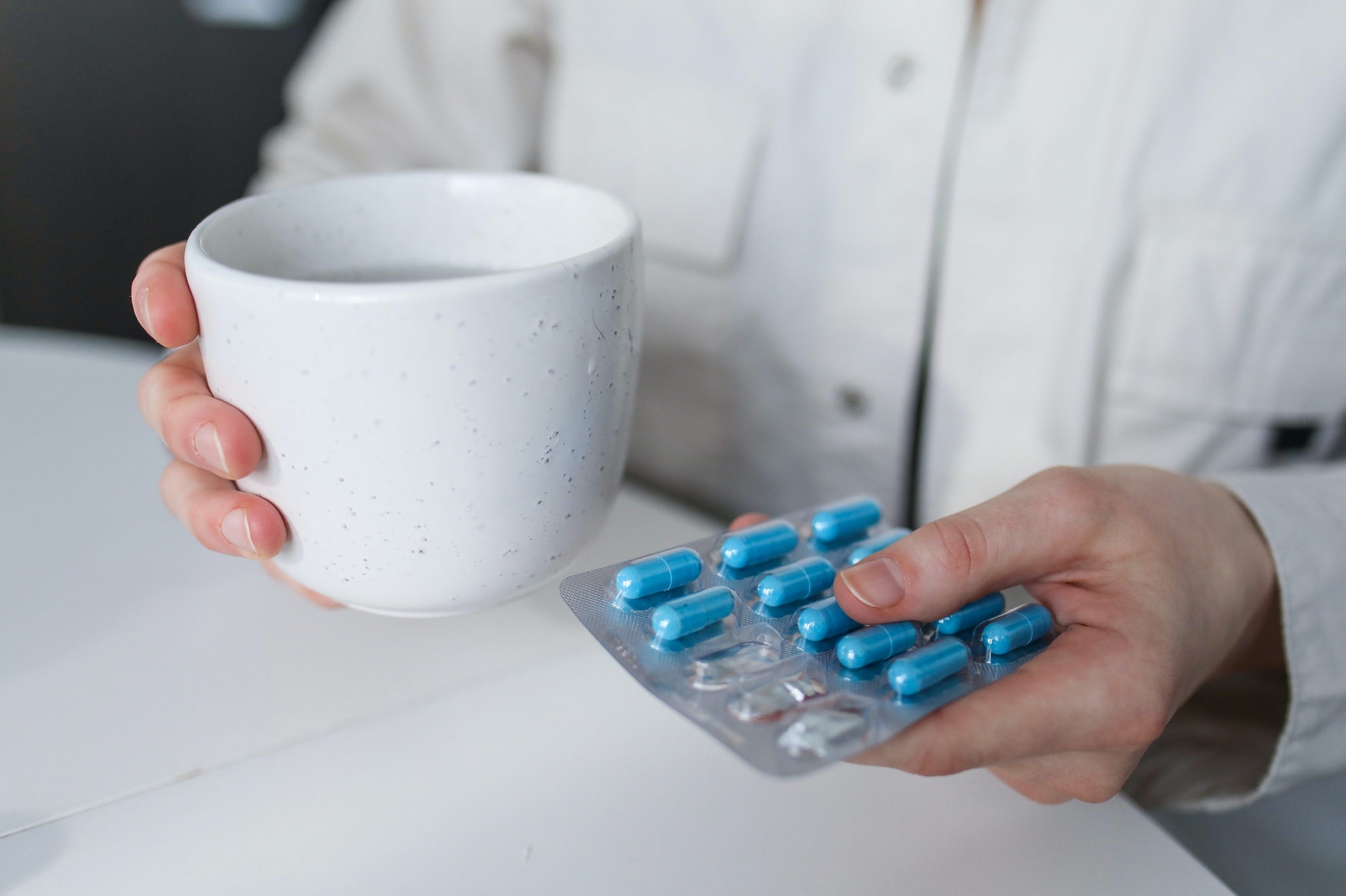 Persona que sostiene una taza y un paquete de pastillas