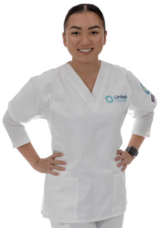 A nursing student in white scrubs, smiling with hands on her hips.