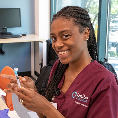A nursing student in maroon scrubs preparing a shot
