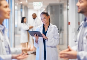 Enfermera sonriendo ante una tableta en el pasillo de un hospital