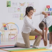 Smiling physical therapist assistant helping a boy perform exercises