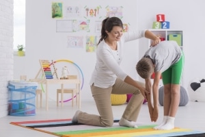 Smiling physical therapist assistant helping a boy perform exercises