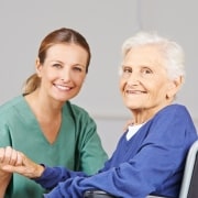 Elderly woman in a wheelchair grasping the hand of a physical therapist assistant