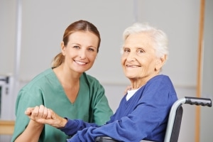 Anciana en silla de ruedas agarrando la mano de un asistente de fisioterapeuta