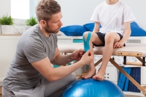 Physical therapy professional applying medical tape to a young patient