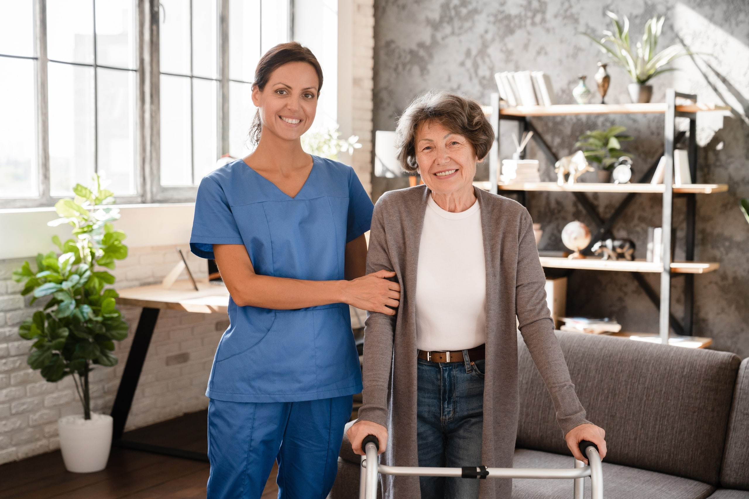 Nurse in scrubs standing next to an elderly woman using a walker